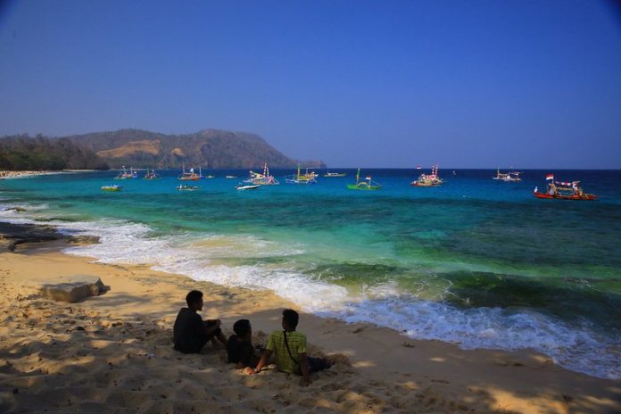 Beberapa remaja masyarakat Mantehage sedang bersantai dengan tenang di pinggir pantai berpasir putih dengan air laut yang jernih.